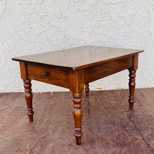 Può includere: Un tavolo in legno marrone scuro con un cassetto e gambe tornite. Il tavolo ha una superficie liscia e lucida.
