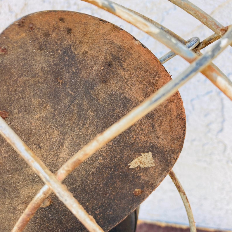 Pu&ograve; includere: Primo piano di una ventola in metallo arrugginito con una pala circolare marrone. La ventola &egrave; realizzata in filo metallico e ha un design semplice.