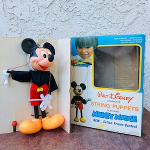 May include: Vintage Walt Disney Mickey Mouse string puppet in a box. The puppet is black and red with yellow shoes. The box has a picture of Mickey Mouse on it and says "New...Action Frame Control".