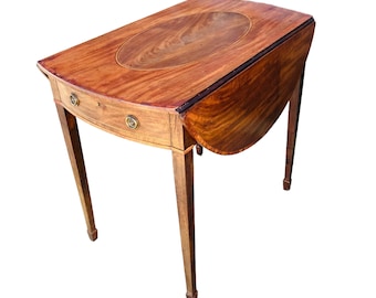 May include: A mahogany drop-leaf table with a rounded oval top and a single drawer. The table has four turned legs and brass hardware.