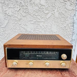 Puede incluir: Sintonizador FM estéreo McIntosh MR67 vintage con tapa de madera y placa frontal dorada. El sintonizador tiene una pantalla negra con letras blancas y varias perillas. La parte superior tiene una rejilla estampada.