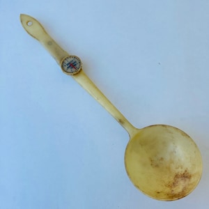 May include: A white plastic ladle with a round bowl and a long handle. The handle has a small, round, white dial with black markings and a red needle.