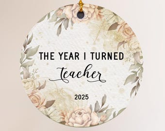 May include: A round porcelain ornament with a floral design and the text "THE YEAR I TURNED teacher 2025". The ornament is 3" x 3" and has a gold string for hanging.