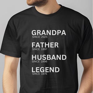 May include: Black t-shirt with white text on the front that reads "Grandpa since 2025, Father since 1997, Husband since 1996, Legend since 1975". The back of the shirt has white text that reads "Mike 50".