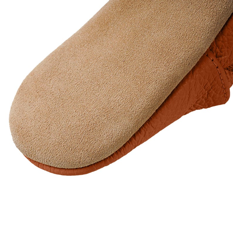 May include: Close-up of a brown leather moccasin with a suede sole. The moccasin has a soft, textured surface and a simple design.