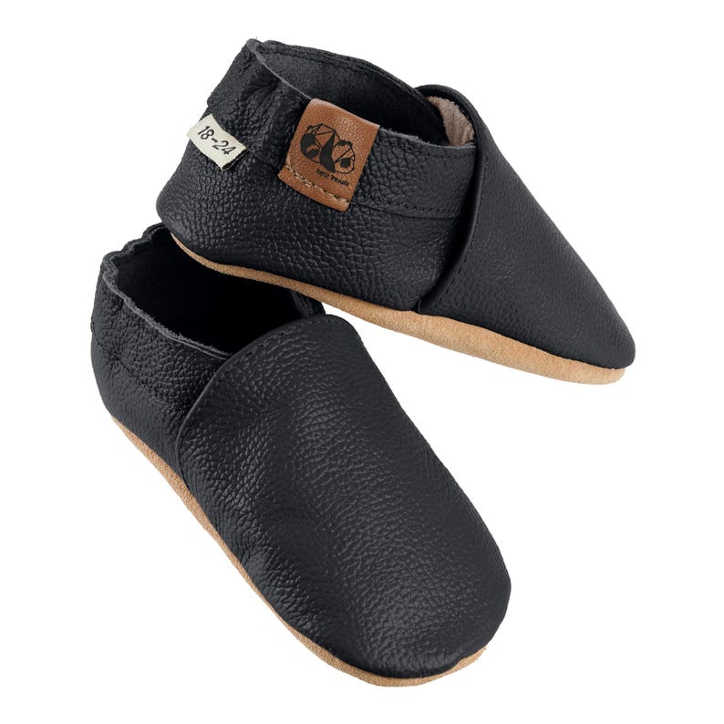 May include: Black leather baby shoes with a brown leather label that says "18-24".