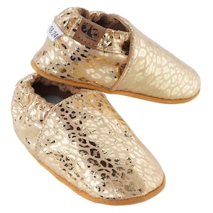 May include: Gold leather baby shoes with a leopard print pattern. The shoes have a soft, flexible sole and are perfect for crawling and walking.