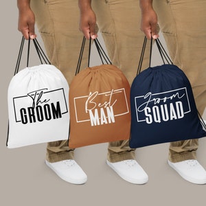 May include: Three white drawstring bags with black text. The bags say "The Groom", "Best Man", and "Groom Squad".