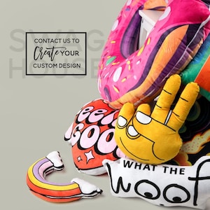 May include: A collection of colourful plush pillows with various designs. The pillows feature a doughnut, a hand with two fingers up, a rainbow, and a pillow with the text "What the woof".