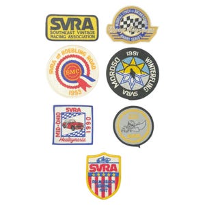 May include: A collection of vintage racing patches with various designs and text. The patches feature the letters "SVRA" prominently, along with other text such as "Southeast Vintage Racing Association," "Mid-Ohio," and "Palm Beach." Colors include yellow, red, blue, and white.