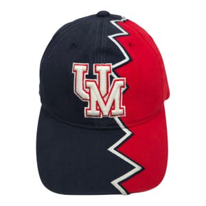 May include: A navy blue and red baseball cap with a white embroidered "UM" logo. The cap features a zig-zag design separating the two colors. The hat is a standard size and has a curved brim.