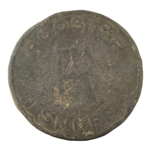 May include: A close-up of a dark gray metal coin with the words "GROSSWORTH" and "ONE CENT" inscribed on it.