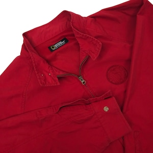 May include: A bright red jacket with a zipper closure and a small embroidered globe emblem. The jacket has a collared neckline and a buttoned cuff. The National Geographic logo is visible on the inside of the collar.