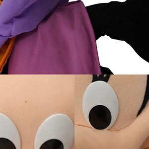 May include: A purple and black plush toy with large white eyes and a black nose. The toy is wearing a purple and orange hat.