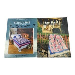 May include: Two books from the "Quilt in a Day" series. The book on the left is titled "Flying Geese Quilt in a Day" and the book on the right is titled "May Basket". Both books feature colourful quilt designs and are by Eleanor Burns.