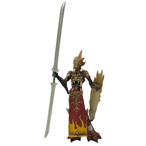May include: A red and gold action figure of a warrior with a large sword and a shield. The figure has a dragon-like head and is wearing a red and gold robe.