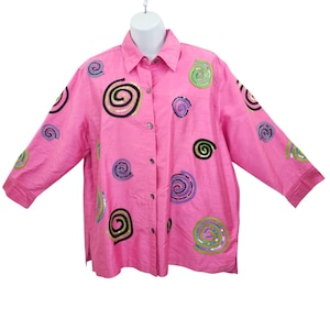 Puede incluir: Una camisa rosa brillante con botones y mangas tres cuartos. La camisa está decorada con diseños de espirales bordadas en lentejuelas negras, verdes, moradas y doradas. Tiene cuello camisero y un corte holgado.