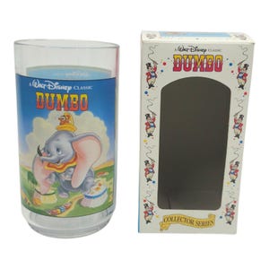 Puede incluir: Un vaso transparente con una ilustración colorida de Dumbo, el elefante de la película de Disney. El vaso tiene un fondo azul con las palabras "A Walt Disney Classic Dumbo". Junto a él, una caja de coleccionista a juego.