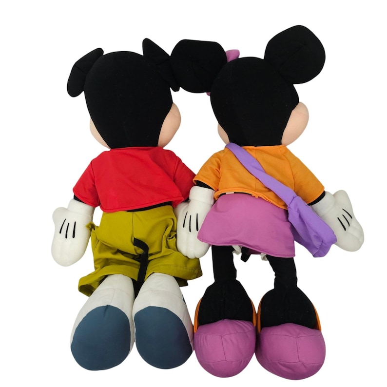 May include: A plush Mickey Mouse and Minnie Mouse toy set. Mickey is wearing a red shirt, yellow pants, and black shoes. Minnie is wearing an orange shirt, purple skirt, and purple shoes.