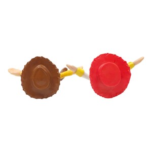 May include: Overhead view of two toy cowboy hats, one brown and one red, with outstretched arms. The brown hat has a wide brim and a rounded crown. The red hat has a smaller brim and a flat top. Both have yellow details.