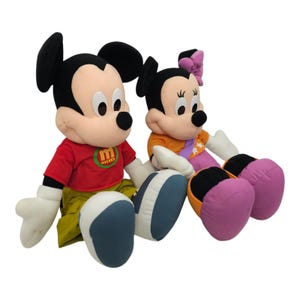 May include: A plush Mickey Mouse and Minnie Mouse toy set. Mickey is wearing a red shirt with the word "Mickey" on it and Minnie is wearing an orange shirt with a purple bow.