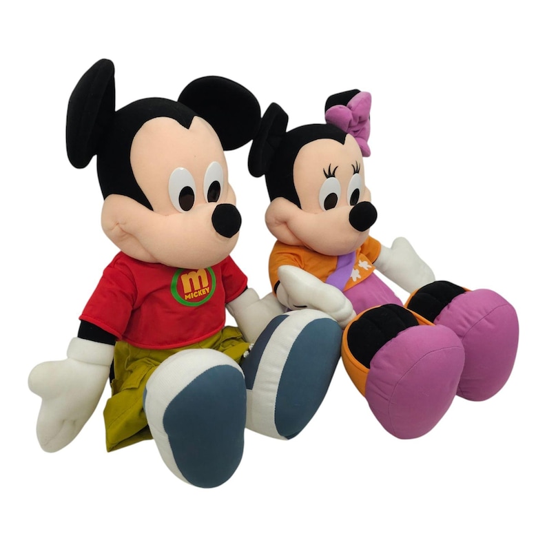 May include: A plush Mickey Mouse and Minnie Mouse toy set. Mickey is wearing a red shirt with the word "Mickey" on it and Minnie is wearing an orange shirt with a purple bow.