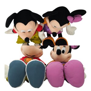 May include: Four plush toys of Mickey Mouse and Minnie Mouse characters. The toys are all wearing different outfits. Mickey Mouse is wearing a red shirt and green pants. Minnie Mouse is wearing a purple shirt and orange pants. The other two toys are wearing a red shirt with a yellow "M" and a purple shirt with a yellow "M".