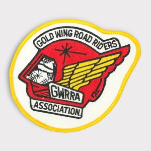 Puede incluir: Un parche bordado blanco y amarillo con el texto "Gold Wing Road Riders Association" y un gráfico de casco alado rojo y amarillo.