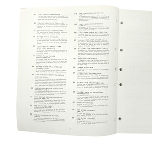May include: Open textbook pages with technical titles like "The Autotransformer," "Three Phase Circuits," and "Synchronous Motor." The pages are white with black text and a few small illustrations. The book is open to a spread.