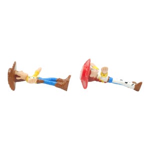 May include: Two toy figurines of characters from the animated film Toy Story. One figure is Woody, wearing a brown cowboy hat, yellow shirt, blue trousers, and brown boots. The other is Jessie, with a red hat, yellow shirt, and blue trousers.