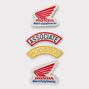 May include: Three embroidered patches. The top patch is red and white with the Honda logo and the text "Honda Rider's Club of America". The middle patch is red with white text that says "Associate". The bottom patch is yellow with white text that says "Booster".