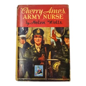 May include: A vintage book cover for "Cherry Ames, Army Nurse" by Helen Wells. The cover shows a woman in a military uniform waving, with other figures in the background. The title is in a bold, red font, and a postage stamp is affixed to the cover.