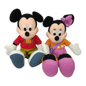 May include: Two plush toys of Mickey Mouse and Minnie Mouse. Mickey is wearing a red shirt with the letter "M" and the word "Mickey" on it. Minnie is wearing a yellow and orange dress with white flowers and a purple sash. Both toys have black shoes.