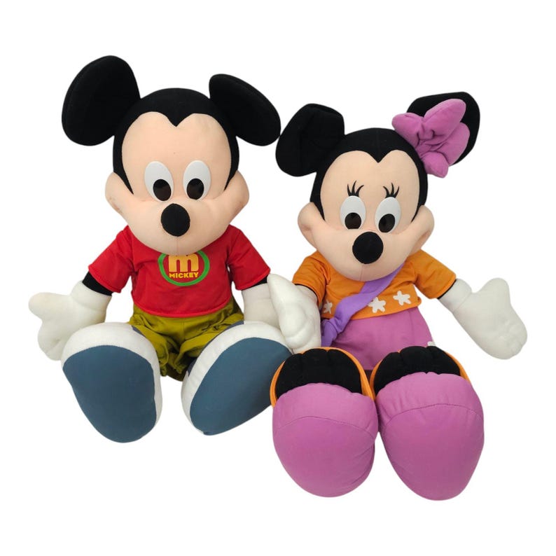 May include: Two plush toys of Mickey Mouse and Minnie Mouse. Mickey is wearing a red shirt with the letter "M" and the word "Mickey" on it. Minnie is wearing a yellow and orange dress with white flowers and a purple sash. Both toys have black shoes.