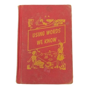 May include: A red hardcover book titled Using Words We Know with gold embossed illustrations on the front cover. The design features a picnic scene with two figures, a basket, and a tree, all rendered in a metallic gold color against the red.