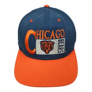 Puede incluir: Gorra de béisbol de los Chicago Bears en azul marino y naranja. La gorra presenta el logotipo del equipo y la palabra "CHICAGO" bordada en naranja. La visera es naranja y la corona azul marino.