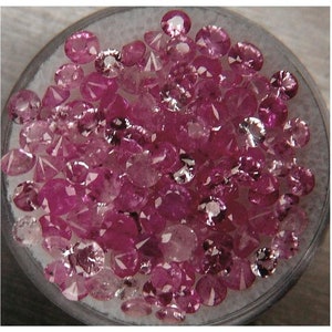 Pode incluir: Uma visão de perto de uma coleção de pedras preciosas cor-de-rosa soltas em um recipiente transparente. As pedras preciosas são de vários tamanhos e formas, algumas têm uma forma mais oval e outras são mais redondas.