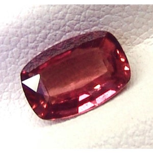 May include: A deep red gemstone with a rectangular shape and a slightly rounded edge. The gemstone is cut and polished, and it has a smooth, shiny surface.