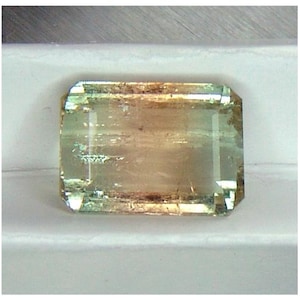 May include: A light green and brown gemstone with a rectangular shape and faceted edges.