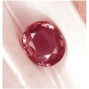 May include: A deep red oval gemstone with a faceted cut.
