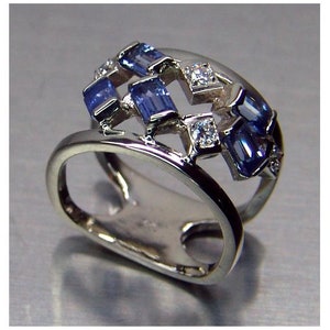 Op de afbeelding: Een zilveren ring met een ontwerp van blauwe en witte edelstenen. De ring heeft een uniek, opengewerkt ontwerp met meerdere banden.