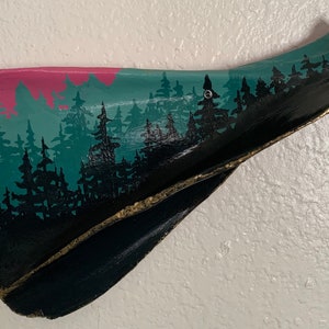 May include: A wooden wall hanging shaped like a mountain range with a painted forest scene. The mountains are painted in shades of pink, teal, and black. The forest is painted in black with a gold accent along the bottom.