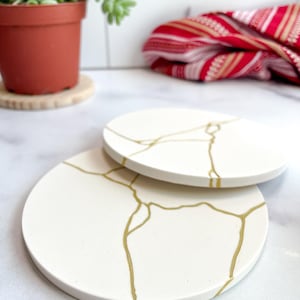 May include: A white ceramic mug with a black handle and the text "But First, Coffee" in a black, bold font. The mug is sitting on a wooden surface. The mug is a standard size.