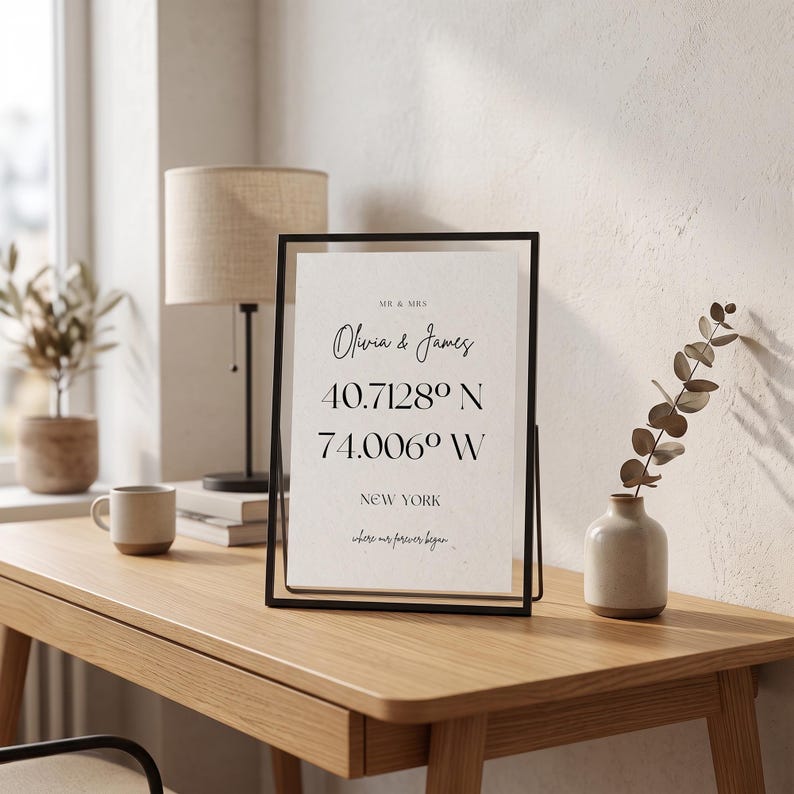 May include: A rectangular black metal frame holding a white print with the text MR & MRS, Olivia & James, 40.7128&deg; N, 74.006&deg; W, NEW YORK, and where our forever began. The print features black serif and script typography on a textured paper background.
