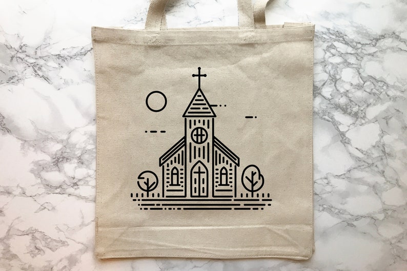 May include: A beige canvas tote bag featuring a black line art illustration of a church building with a steeple, a cross, a circular window, and arched doors. The design includes a sun, two stylized trees, and horizontal ground lines.