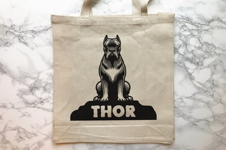 May include: A beige tote bag with black handles and a black and white illustration of a dog sitting on a rock with the word "THOR" printed below it.
