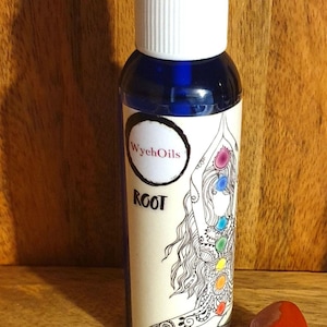 Puede incluir: Una botella de vidrio azul con una etiqueta blanca que dice "WychOils" y "ROOT". La etiqueta también presenta una ilustración en blanco y negro de una mujer con un diseño de chakra arcoíris. Una pequeña tarjeta marrón con texto escrito a mano está al lado de la botella. El texto dice "Raíz, Pachulí, Incienso, Cedro, Jaspe rojo". También hay una piedra roja al lado de la botella.