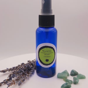 Könnte beinhalten: Eine blaue Glasflasche mit schwarzem Sprühkopf und einem grün-weißen Etikett mit der Aufschrift "WychOils HEART CHAKRA". Um die Flasche herum liegen grüne Steine.