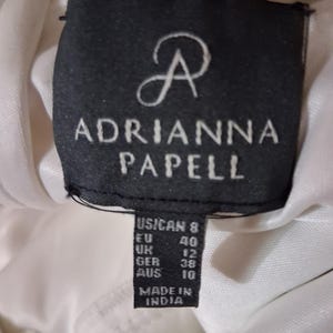 Puede incluir: Primer plano de una etiqueta negra con el texto blanco "ADRIANNA PAPELL". La etiqueta incluye conversiones de tallas para US/CAN, EU, UK, GER y AUS. La etiqueta tambi&eacute;n dice "MADE IN INDIA".