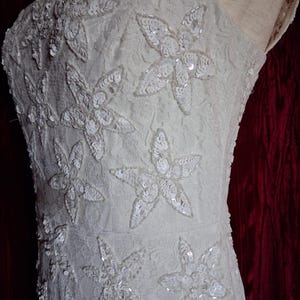 Puede incluir: Vestido color marfil con un dise&ntilde;o floral. El vestido presenta un corpi&ntilde;o ajustado y una delicada capa de encaje. El dise&ntilde;o floral est&aacute; adornado con lentejuelas, a&ntilde;adiendo un toque de brillo. El vestido tiene una silueta simple y elegante, perfecto para ocasiones especiales.